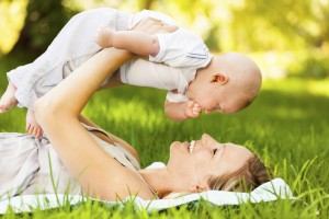 Happy young mother playing with baby boy in garden. Horizontal Shot.